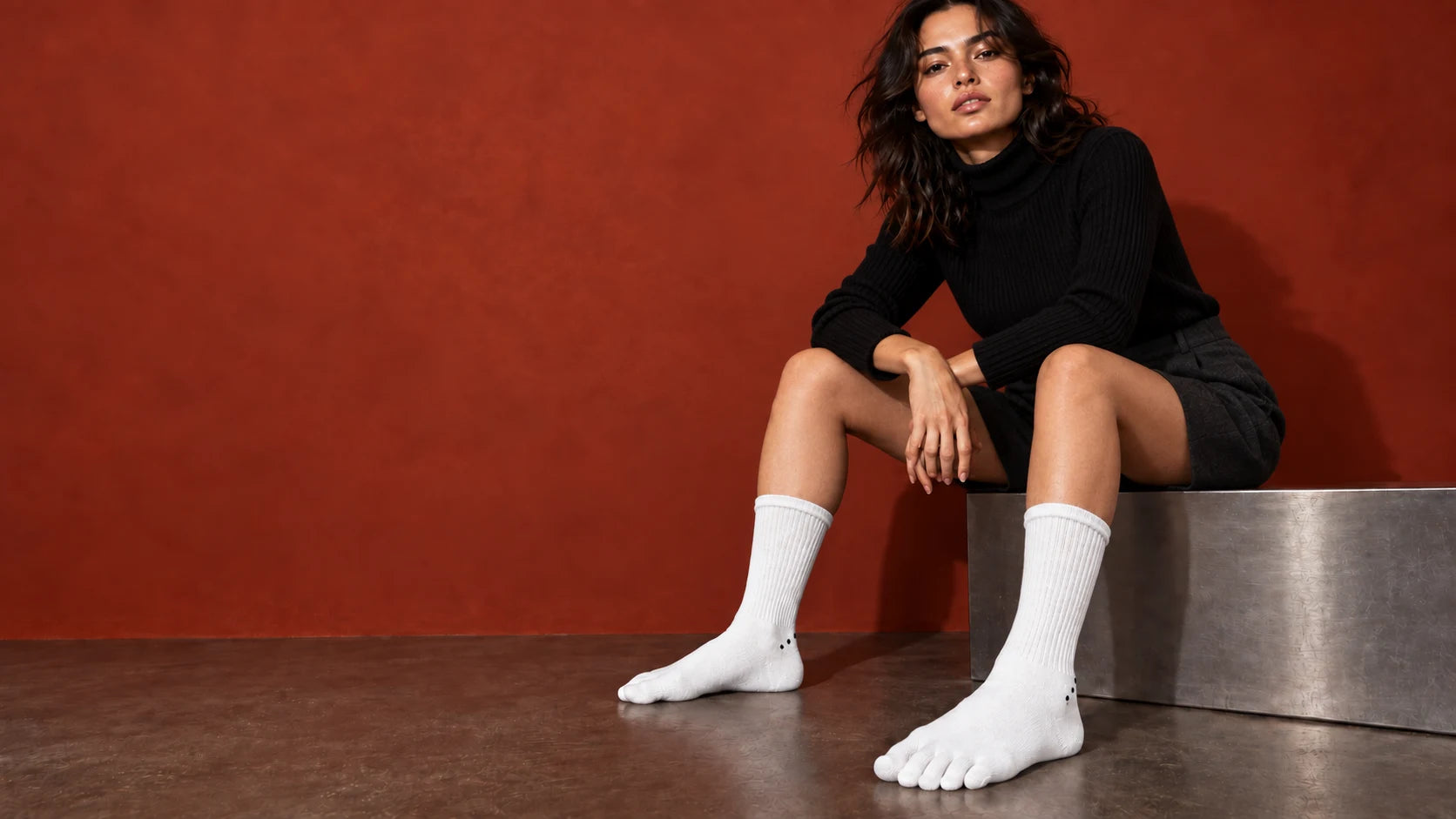 White Albalana five-toe socks, styled with black knitwear in a rust-coloured studio.